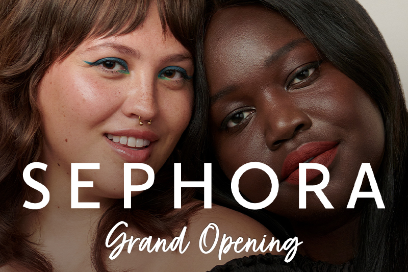 Promotional image for Sephora's Grand Opening featuring two women with makeup close together, one with a teal eyeliner and the other with a coral lipstick, with "SEPHORA Grand Opening" text overlay.