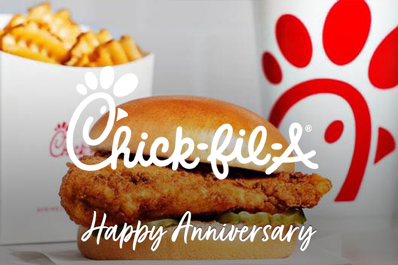 A close-up of a Chick-fil-A chicken sandwich with a golden, crispy fried chicken filet inside a soft, slightly toasted bun with pickle slices. In the background, there's a container of waffle fries and a Chick-fil-A cup with the iconic red logo. Text overlaying the image reads: "Chick-fil-A Happy Anniversary"