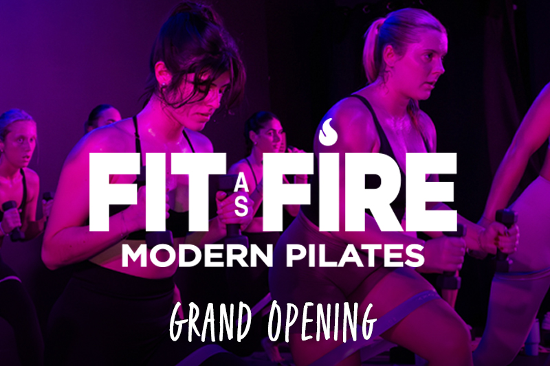 Promotional image for “Fit as Fire Modern Pilates” grand opening, showing several women exercising in a dim studio with pink and purple lighting, using resistance bands and hand weights, with large overlay text reading “Fit as Fire Modern Pilates – Grand Opening.”